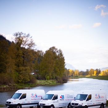 Three white 21 Degrees Hugh's Heating and Air Conditioning vans parked near a river banked with tall trees